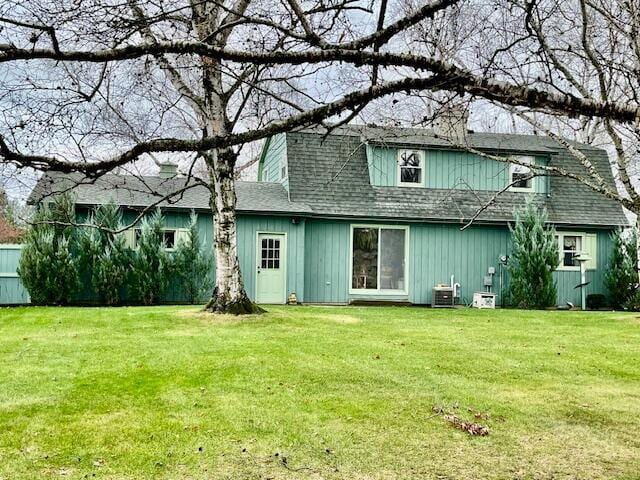 rear view of property featuring a yard, central AC, and roof with shingles