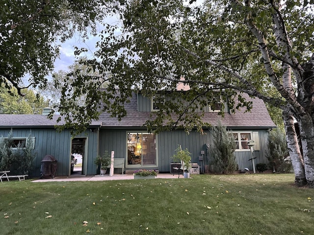 back of property with board and batten siding, a shingled roof, a patio, and a yard