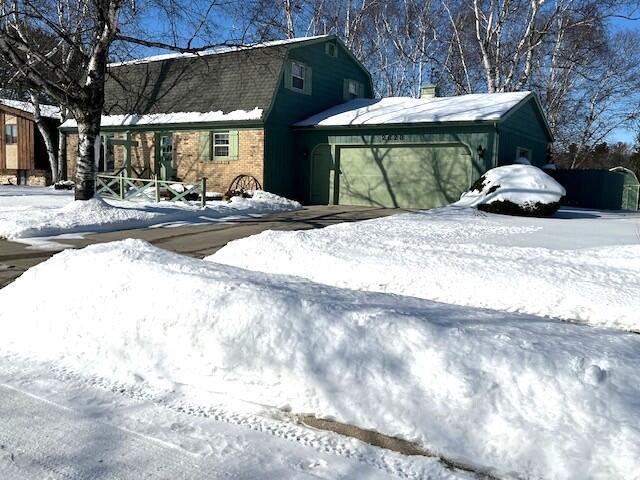 view of snowy exterior with brick siding and a gambrel roof