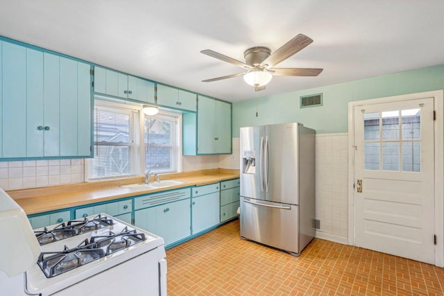 kitchen featuring stainless steel fridge, ceiling fan, white range with gas cooktop, sink, and tile walls