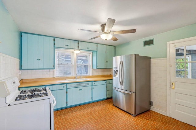 kitchen featuring plenty of natural light, sink, stainless steel refrigerator with ice dispenser, tile walls, and white gas stove