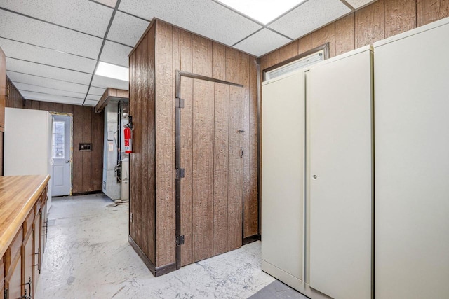 corridor featuring wooden walls and a drop ceiling