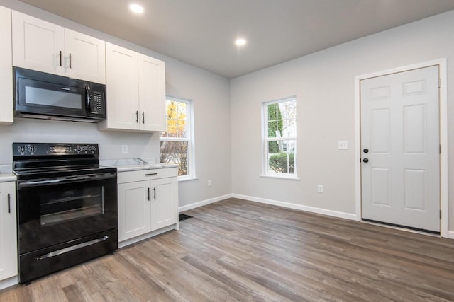 kitchen with light stone countertops, white cabinetry, black appliances, and light hardwood / wood-style floors