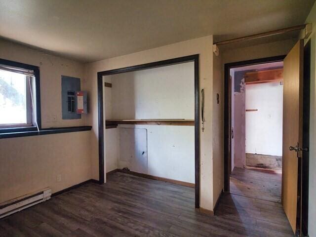 unfurnished bedroom with a baseboard heating unit, electric panel, a closet, and dark wood-type flooring