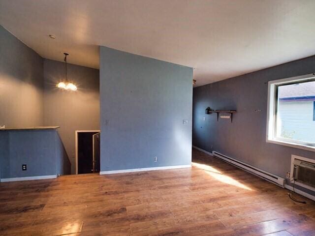 empty room with a baseboard radiator, a notable chandelier, and hardwood / wood-style flooring