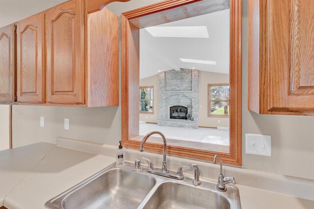 kitchen with light brown cabinetry, sink, a brick fireplace, and vaulted ceiling with skylight