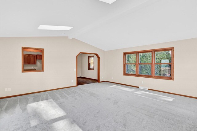 carpeted empty room featuring vaulted ceiling with skylight