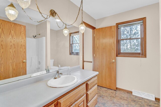 bathroom featuring a shower, vanity, a healthy amount of sunlight, and toilet