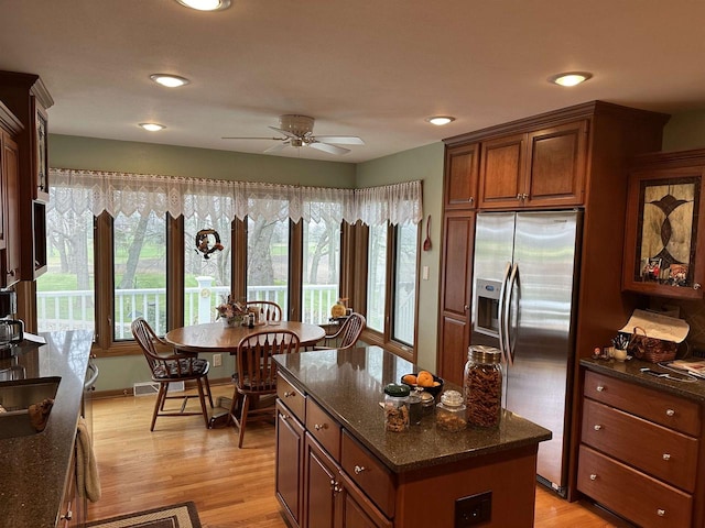 kitchen featuring ceiling fan, a center island, dark stone countertops, stainless steel fridge, and light hardwood / wood-style floors