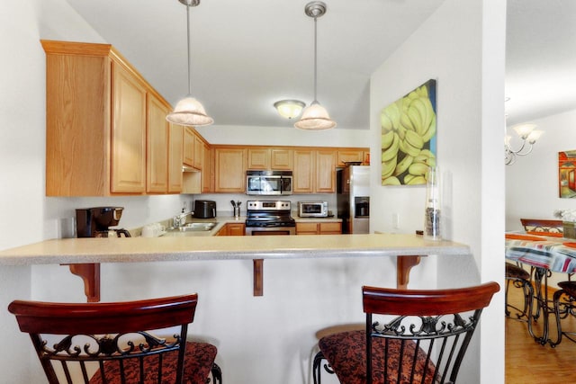 kitchen with a breakfast bar area, light wood-type flooring, a notable chandelier, kitchen peninsula, and stainless steel appliances