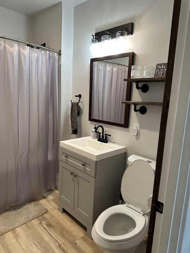 bathroom featuring a textured wall, curtained shower, toilet, wood finished floors, and vanity