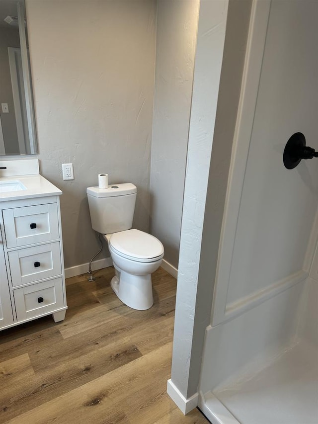 bathroom with toilet, wood finished floors, vanity, baseboards, and a shower