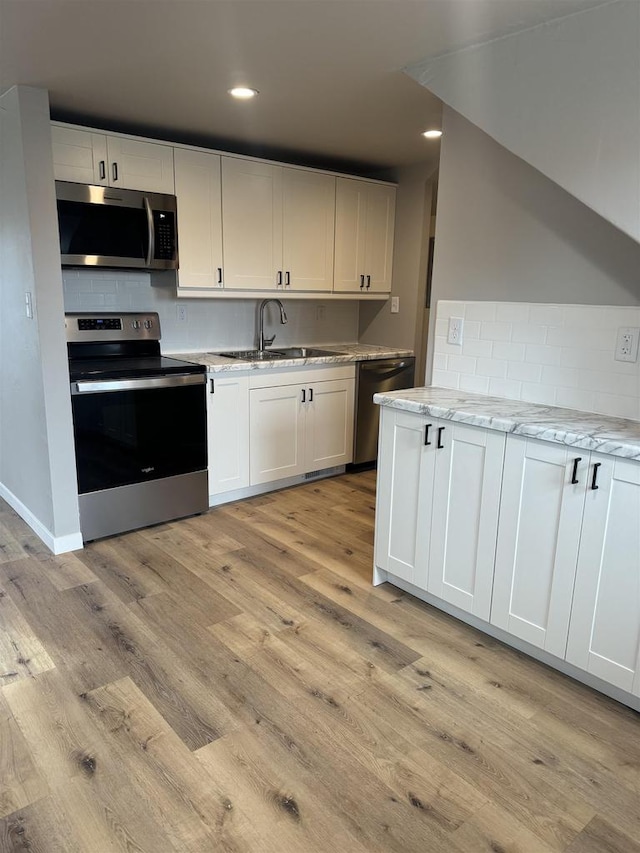 kitchen with light stone countertops, light wood finished floors, appliances with stainless steel finishes, and a sink