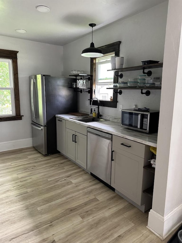 kitchen with light wood finished floors, open shelves, stainless steel appliances, a sink, and baseboards