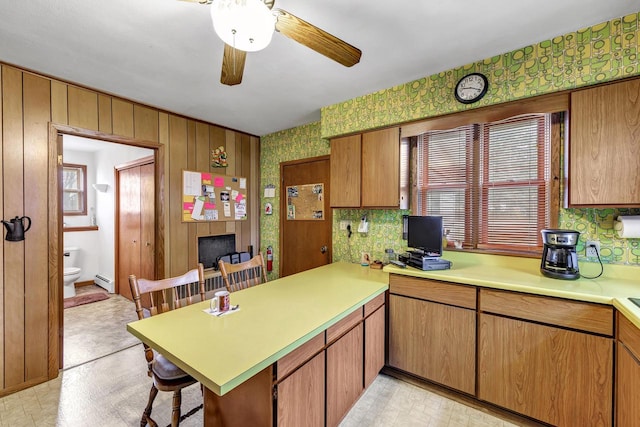 kitchen with ceiling fan, a baseboard radiator, a kitchen breakfast bar, kitchen peninsula, and wood walls