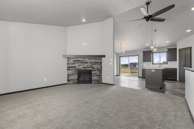 unfurnished living room featuring dark carpet, ceiling fan with notable chandelier, sink, high vaulted ceiling, and a fireplace