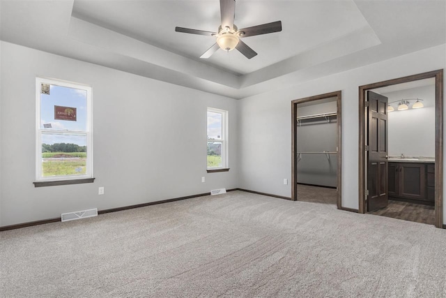 unfurnished bedroom with ensuite bathroom, ceiling fan, a raised ceiling, and multiple windows