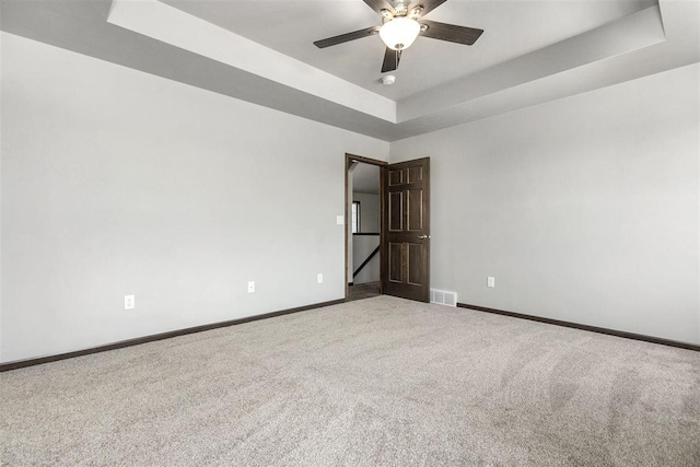 carpeted spare room featuring ceiling fan and a raised ceiling