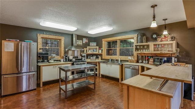 kitchen featuring kitchen peninsula, appliances with stainless steel finishes, wall chimney exhaust hood, dark wood-type flooring, and hanging light fixtures