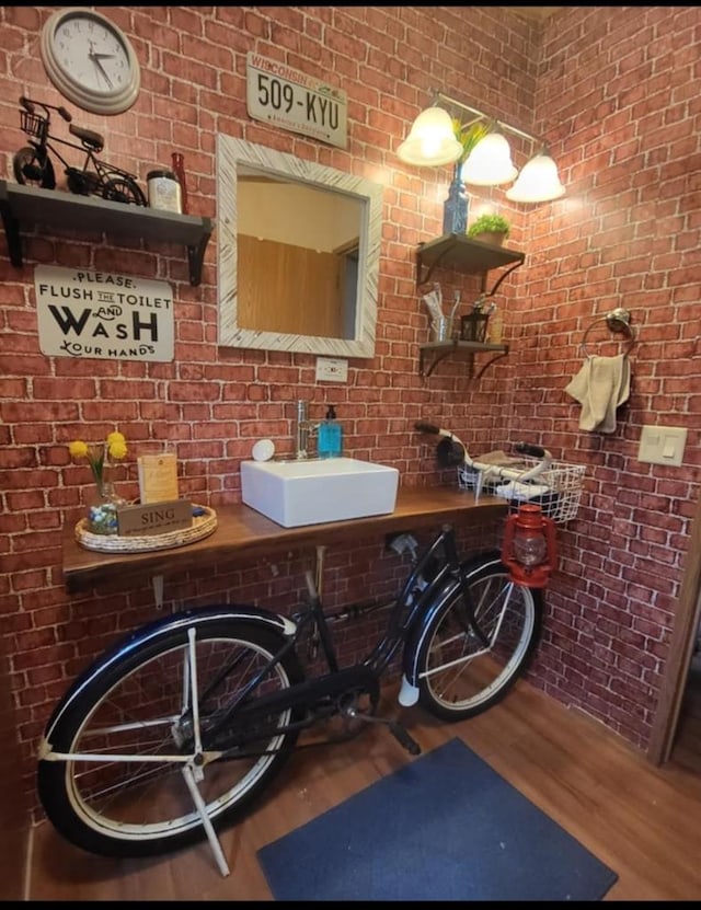 bathroom with hardwood / wood-style floors, sink, and brick wall