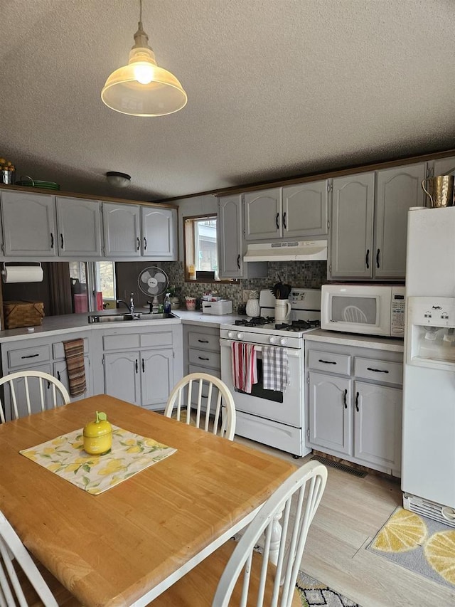 kitchen featuring sink, hanging light fixtures, white appliances, decorative backsplash, and light wood-type flooring