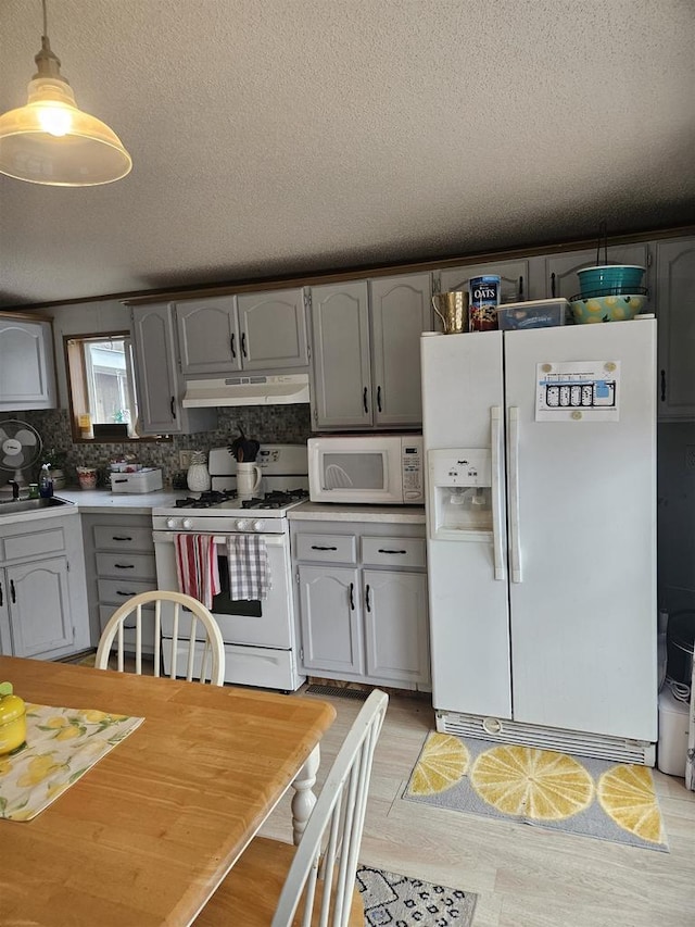 kitchen with a textured ceiling, pendant lighting, white appliances, and light hardwood / wood-style floors