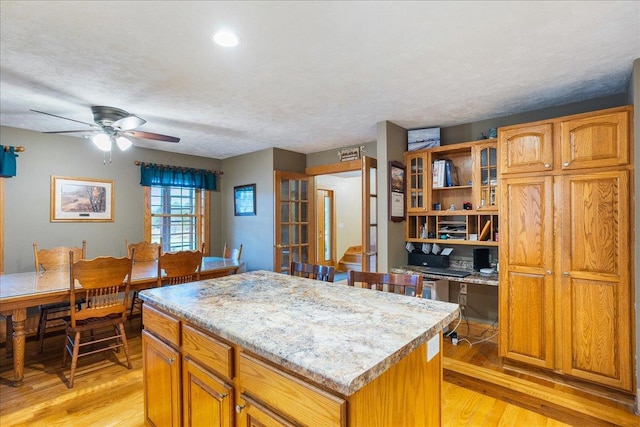 kitchen featuring ceiling fan, a kitchen island, light hardwood / wood-style floors, and a textured ceiling