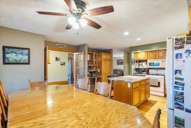 kitchen with a textured ceiling, a center island, white appliances, and light hardwood / wood-style flooring