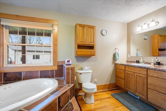 bathroom featuring vanity, a textured ceiling, wood-type flooring, a relaxing tiled tub, and toilet