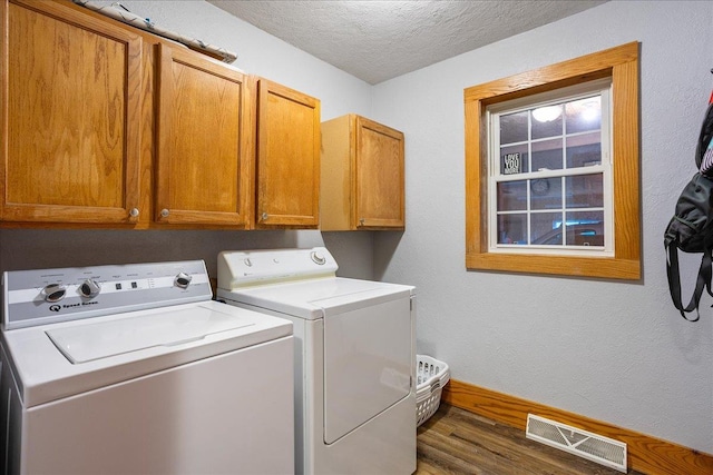 clothes washing area featuring washer and dryer, a textured ceiling, dark hardwood / wood-style floors, and cabinets