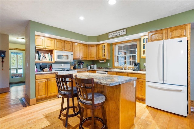 kitchen with light hardwood / wood-style floors, a center island, a kitchen bar, and white appliances