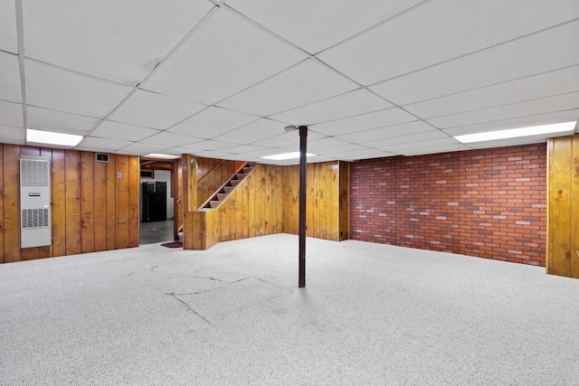 basement with a paneled ceiling, wooden walls, carpet, and brick wall