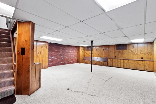 basement with carpet flooring, a drop ceiling, and wood walls