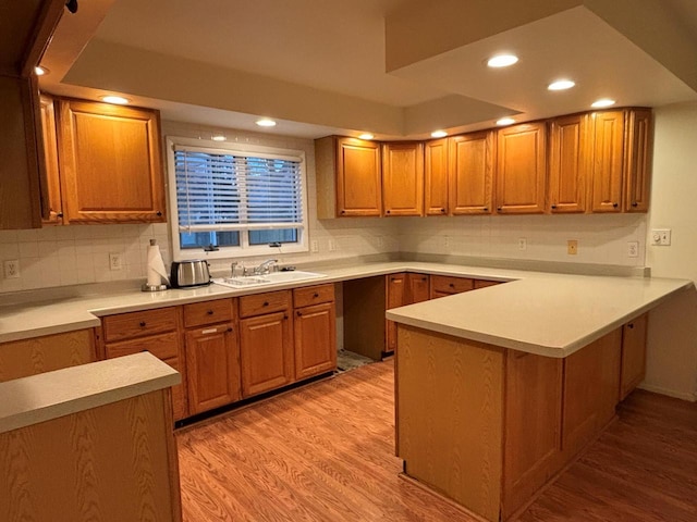 kitchen with kitchen peninsula, decorative backsplash, sink, and light hardwood / wood-style floors