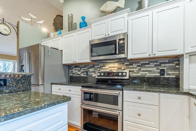 kitchen featuring dark stone countertops, light wood-type flooring, appliances with stainless steel finishes, tasteful backsplash, and white cabinetry