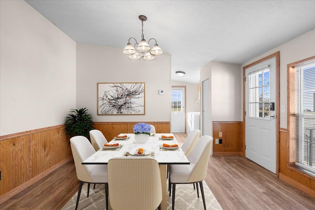 dining area with a textured ceiling, a chandelier, light hardwood / wood-style floors, and wood walls