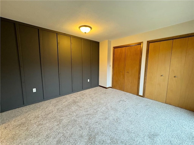 unfurnished bedroom featuring light colored carpet, a textured ceiling, and two closets