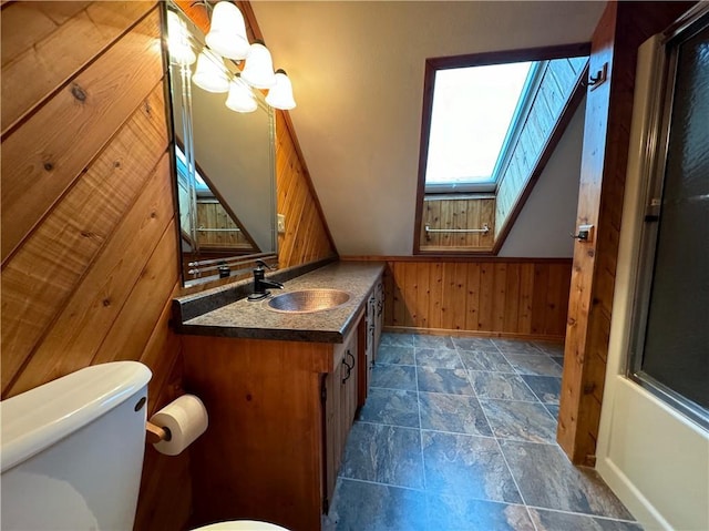 bathroom with a skylight, an inviting chandelier, wood walls, toilet, and vanity