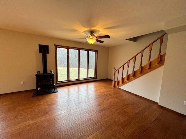 unfurnished living room featuring hardwood / wood-style flooring, ceiling fan, and a wood stove