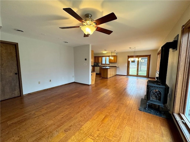 unfurnished living room featuring ceiling fan with notable chandelier, light hardwood / wood-style flooring, and a wood stove