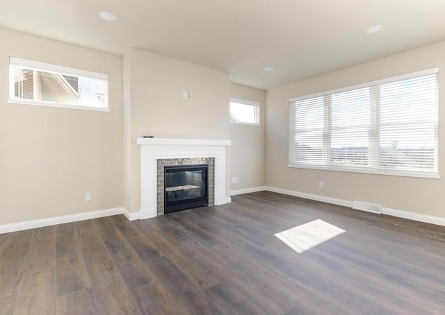 unfurnished living room featuring dark wood-style floors, a tiled fireplace, visible vents, and baseboards