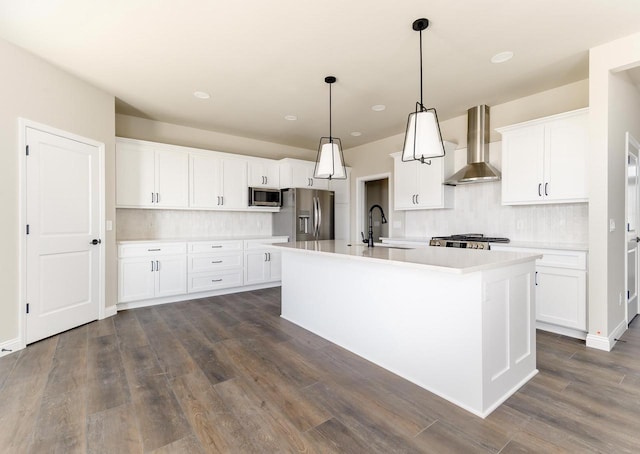 kitchen featuring a center island with sink, stainless steel appliances, light countertops, a sink, and wall chimney exhaust hood