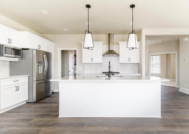 kitchen with stainless steel appliances, light countertops, decorative backsplash, an island with sink, and wall chimney exhaust hood