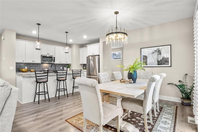 dining area with light hardwood / wood-style flooring, a notable chandelier, and sink