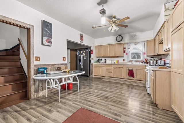 kitchen with white gas stove, stainless steel fridge, light brown cabinetry, and a textured ceiling