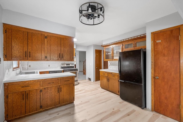 kitchen with backsplash, black fridge, sink, stainless steel electric range oven, and light hardwood / wood-style floors