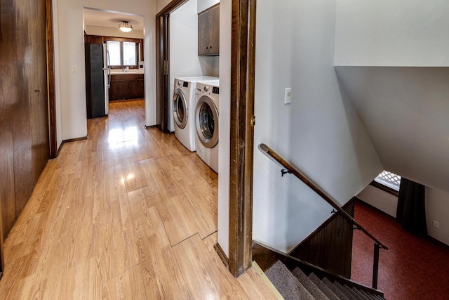 clothes washing area featuring cabinets, sink, separate washer and dryer, and light hardwood / wood-style floors