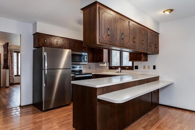 kitchen featuring sink, light hardwood / wood-style flooring, appliances with stainless steel finishes, dark brown cabinets, and kitchen peninsula