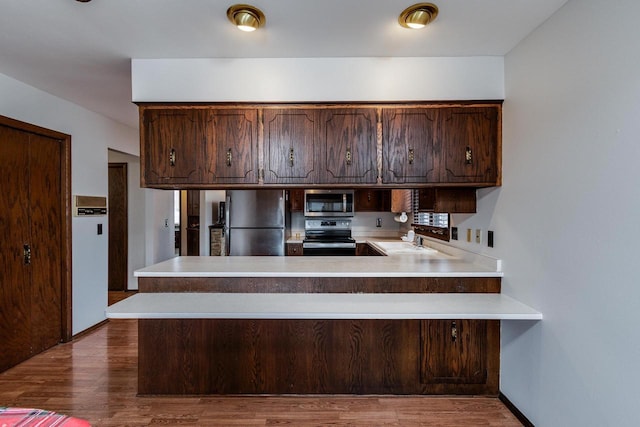 kitchen featuring dark brown cabinetry, stainless steel appliances, kitchen peninsula, and light wood-type flooring