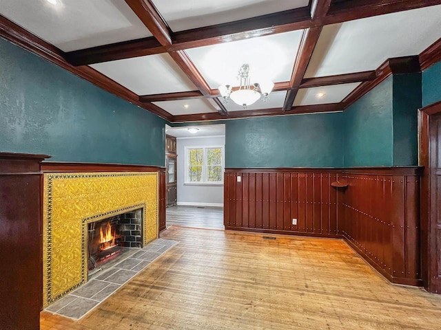 unfurnished living room with coffered ceiling, an inviting chandelier, light hardwood / wood-style flooring, beamed ceiling, and a fireplace